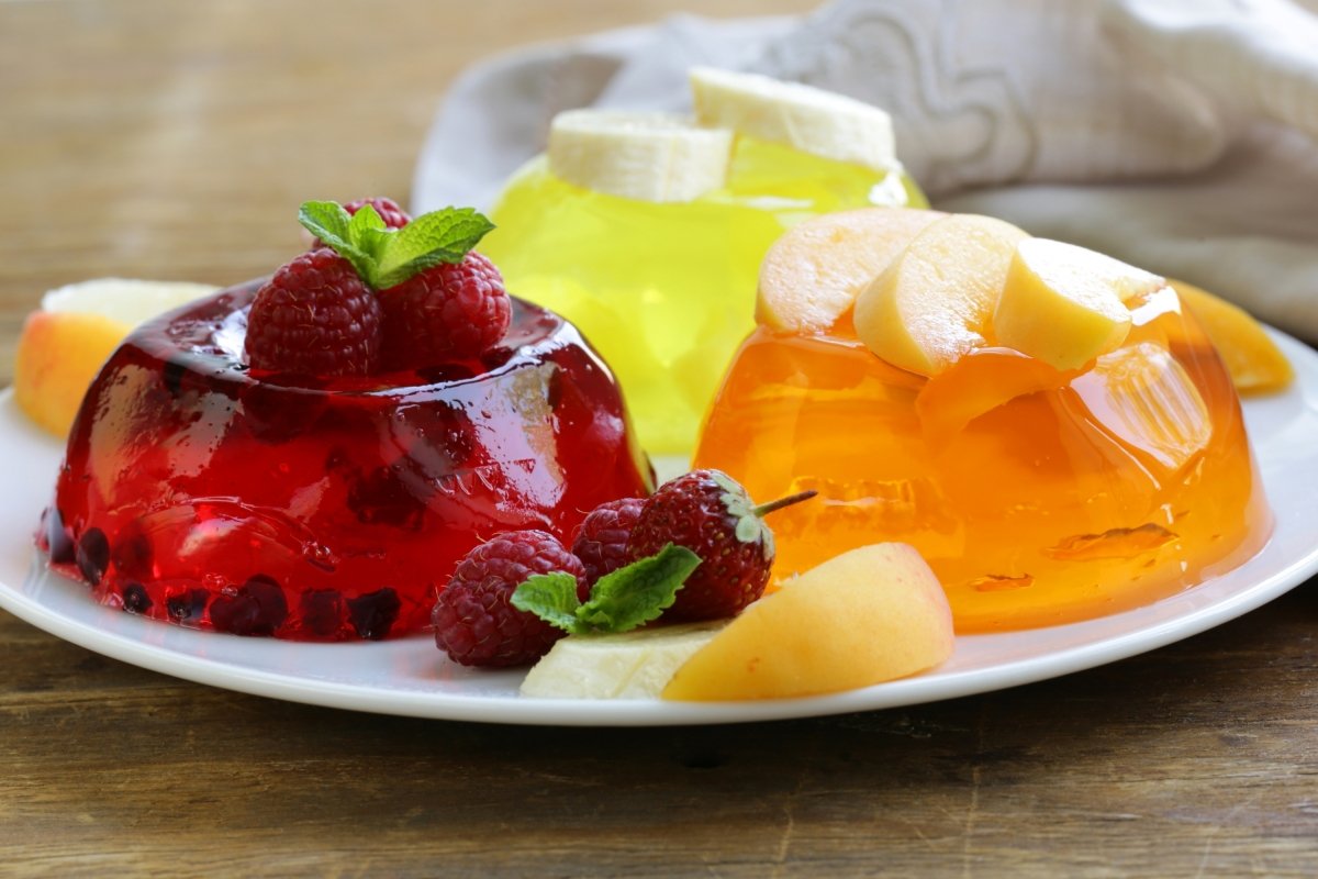 3 gelatinas de diferentes sabores (frambuesa, melocotón, plátano) sobre un plato y algunas frutas alrededor