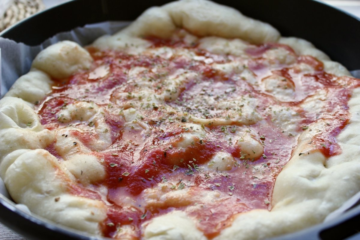 Adición de la salsa de tomate sobre la masa de pizza cocida