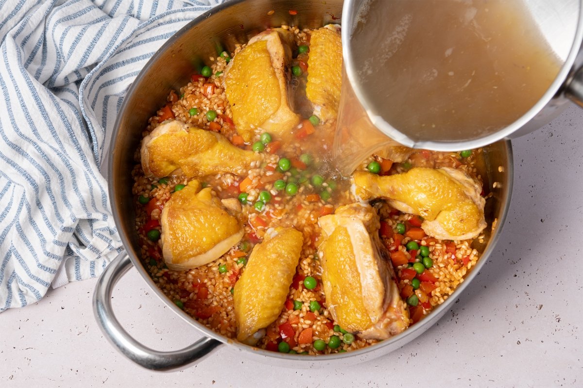 Adición del caldo de pollo y los trozos de pollo dorados para hacer el arroz con pollo