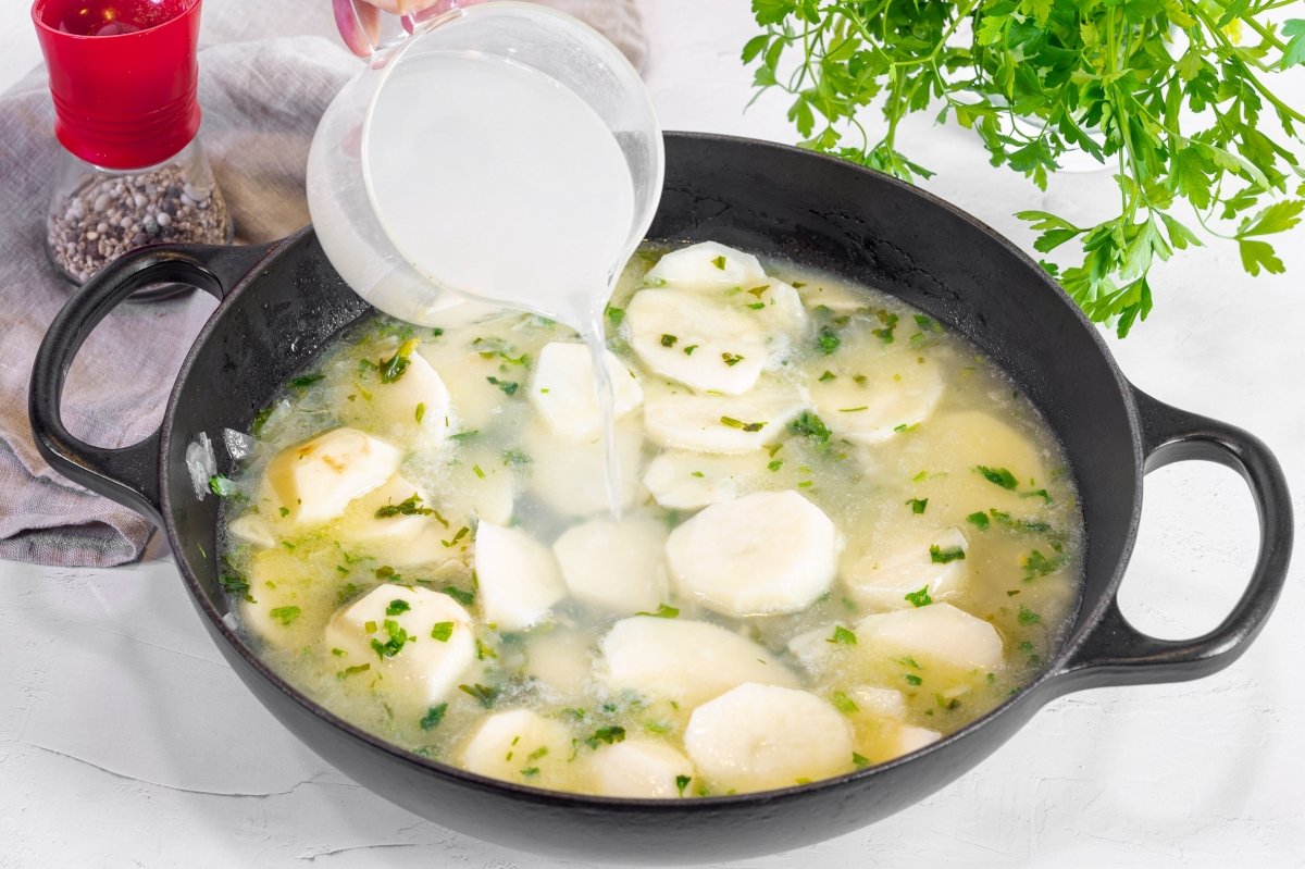 Añadiendo caldo de pescado para hacer patatas en salsa verde