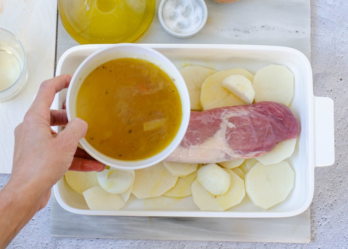 Añadiendo el caldo de carne al solomillo de cerdo al horno con patatas