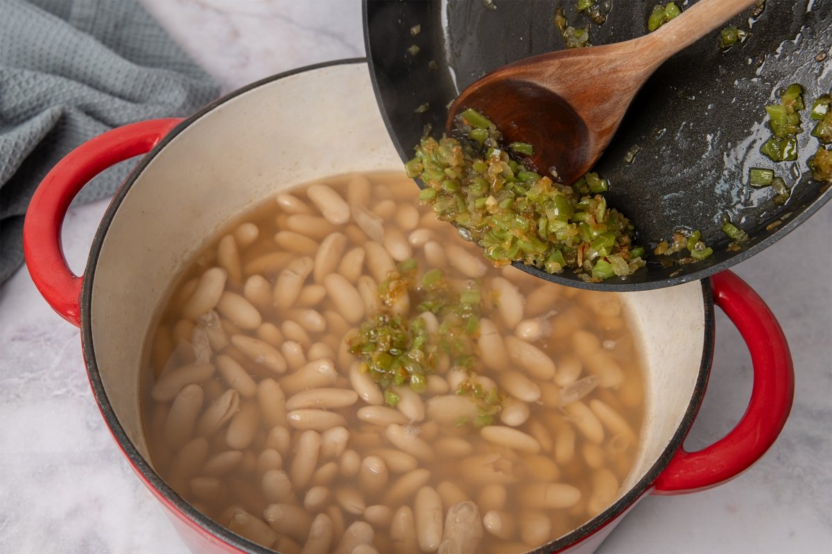 Añadiendo el sofrito a la olla de alubias con almejas