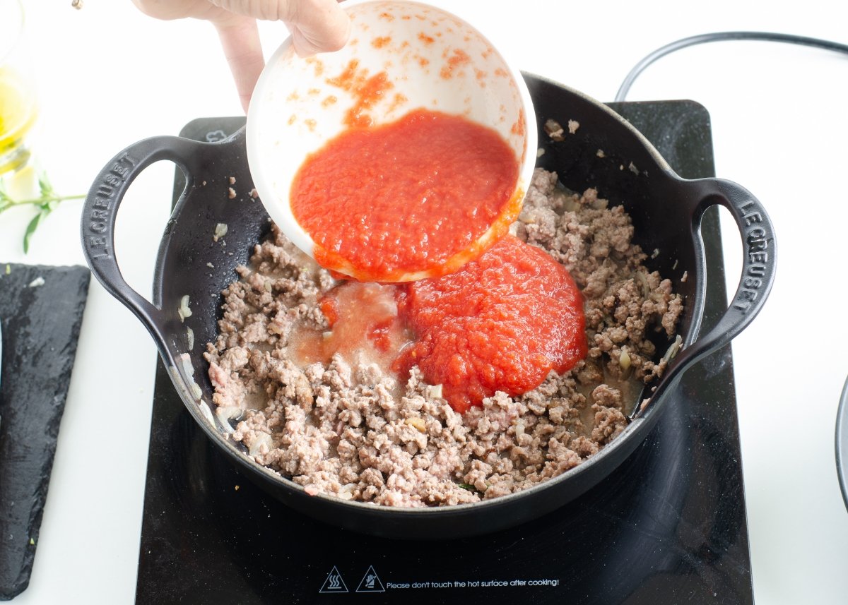 Añadiendo el tomate al relleno para hacer canelones de carne