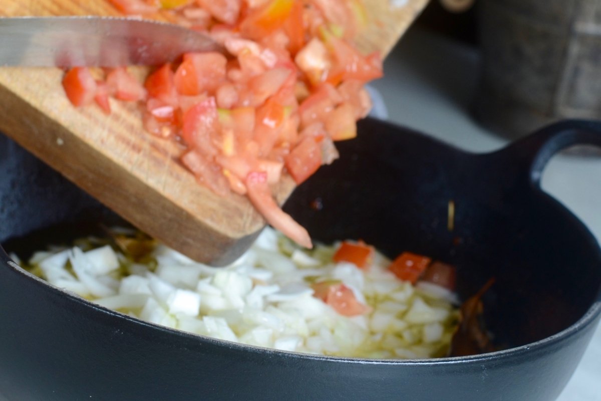 Añadiendo el tomate y la cebolla a la sartén para la empanada de bonito