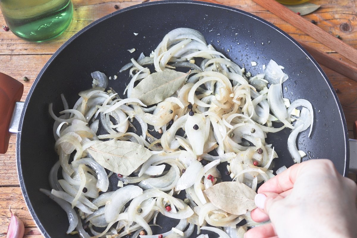 Añadiendo laurel y granos de pimienta a la sartén con cebolla