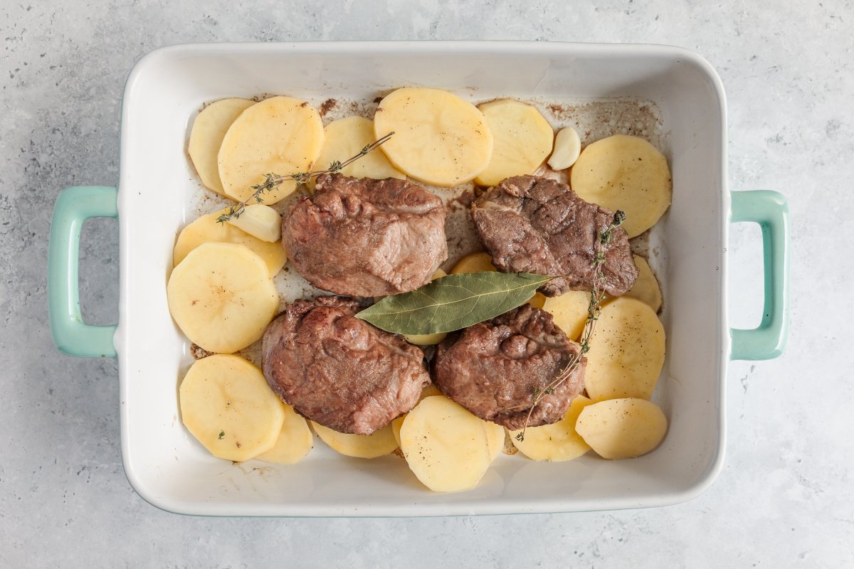 Añadiendo patatas a las carrilleras de cerdo al horno