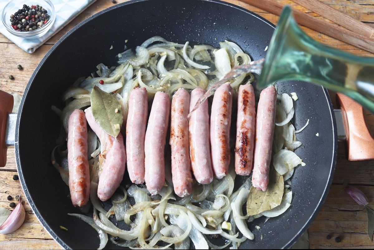 Añadiendo vino blanco a la sartén con las longanizas y la cebolla