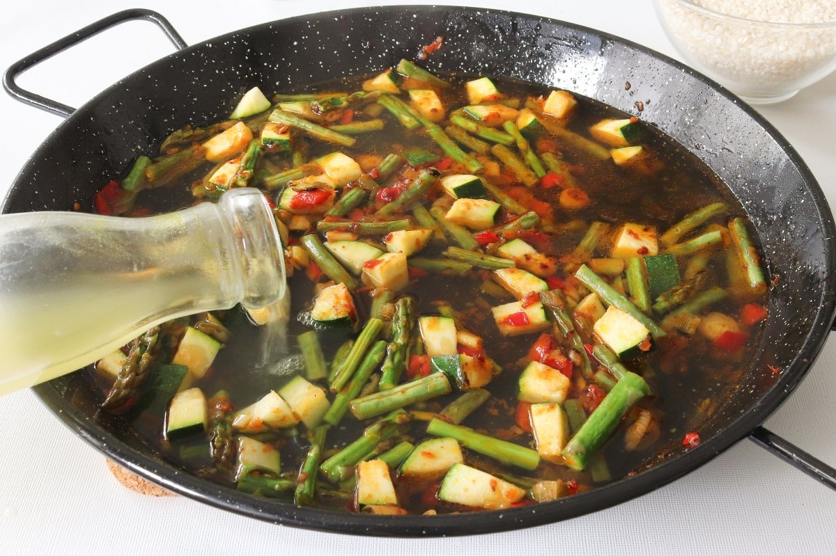 Añadir el caldo a la paella de verduras