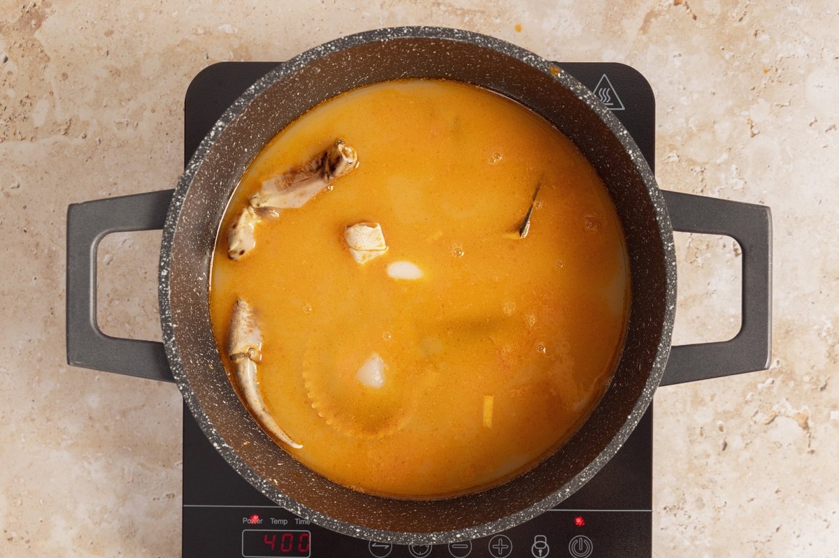 Añadir el caldo de pescado, los calamares, las vieiras, mejillones y el cangrejo a la olla