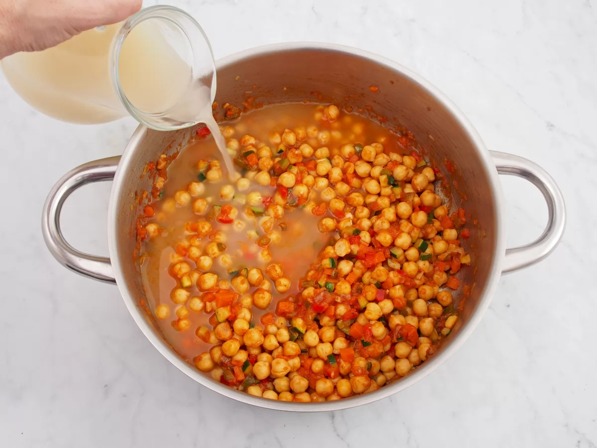 Añadir el caldo de pollo para cocinar los garbanzos guisados