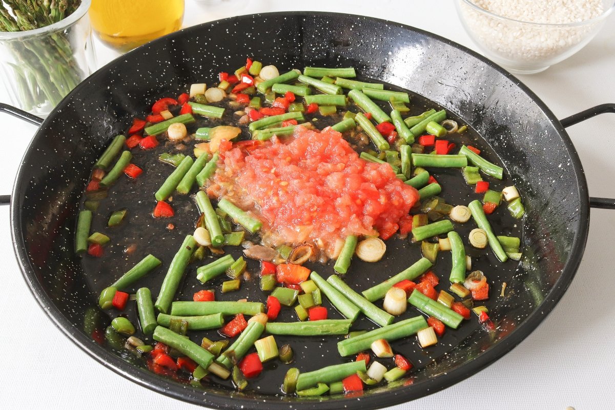 Añadir el tomate rallado a la paella de verduras