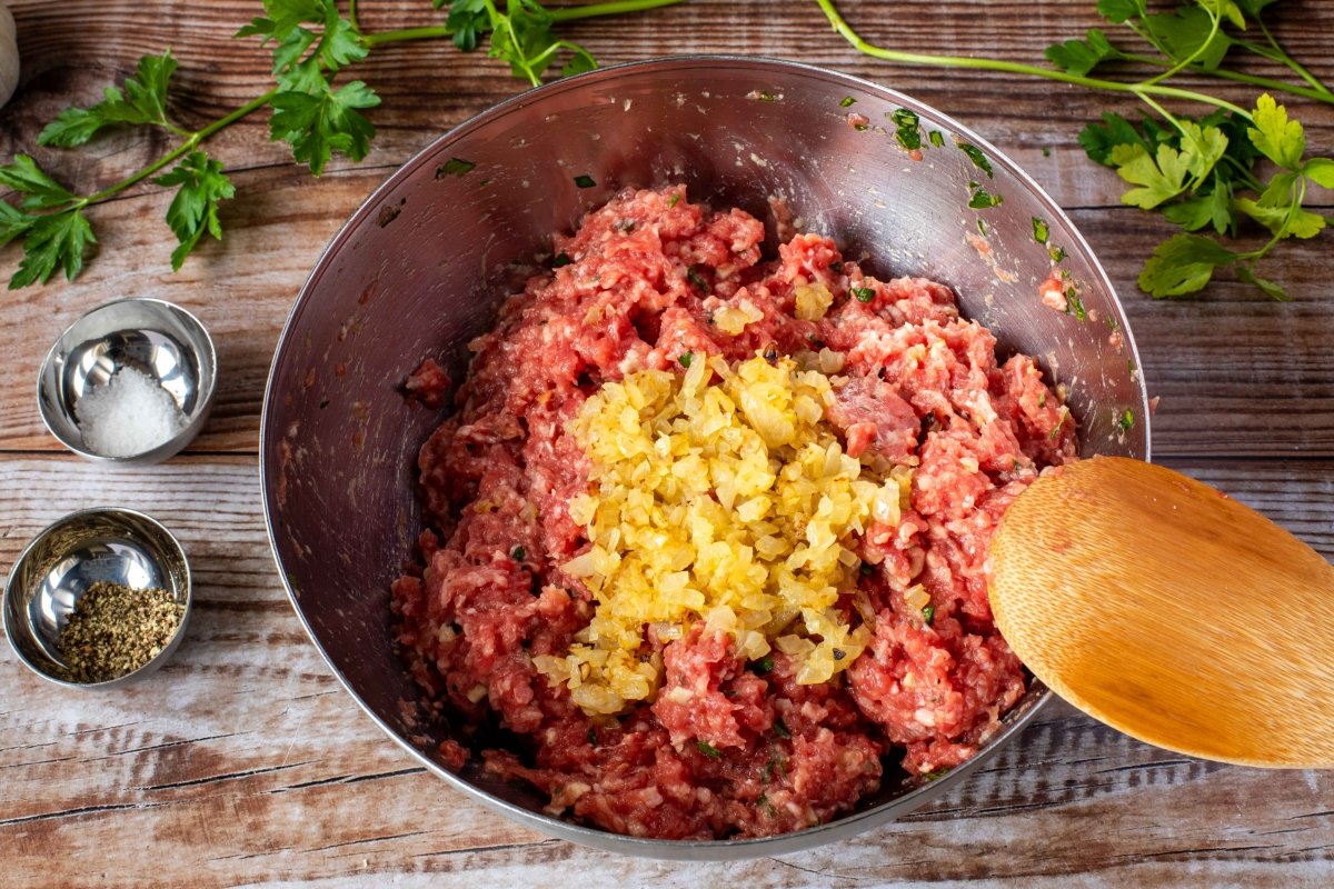 Añadir la cebolla pochada a la carne condimentada para hacer las albóndigas de carne en salsa