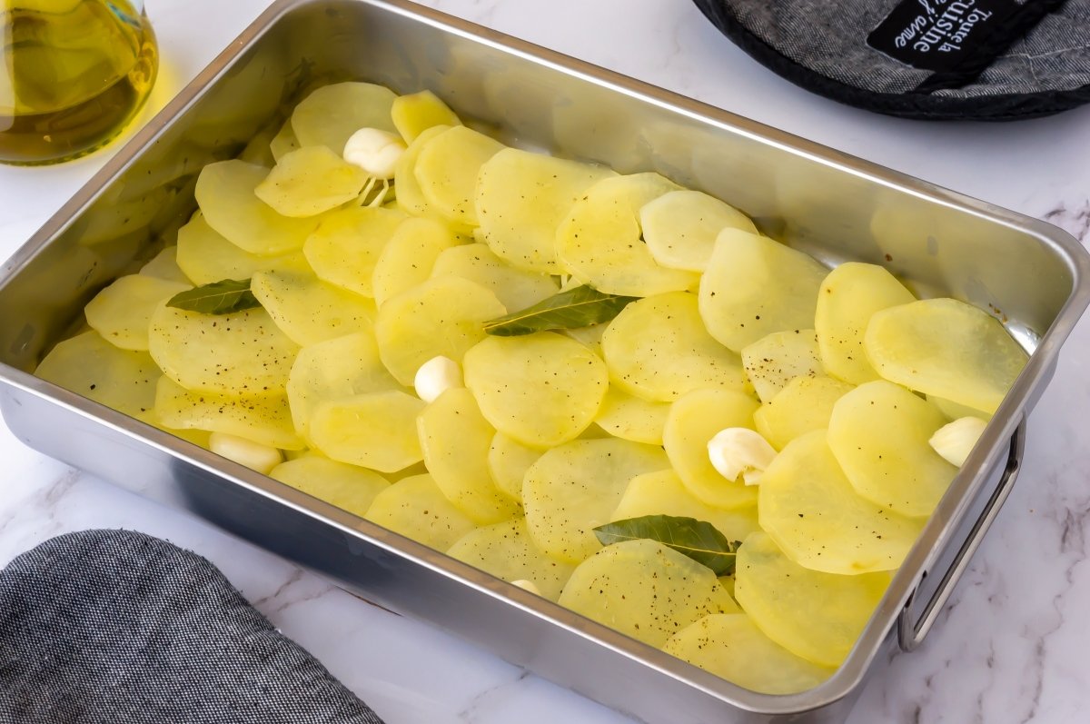 Añadir laurel y ajo a las patatas para la meluza al horno