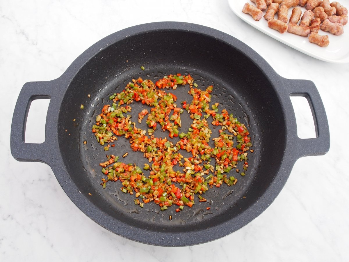 Añadir los pimientos al sofrito del arroz con salchichas