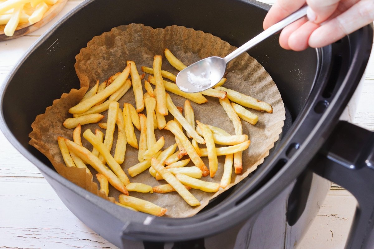 Añadir sal a las patatas fritas congeladas en freidora de aire