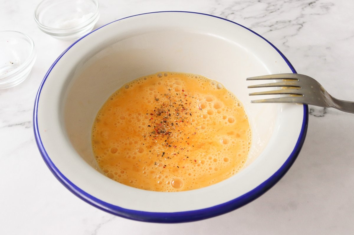 Añadir sal y pimienta a los huevos para la tostada de huevos revueltos con jamón
