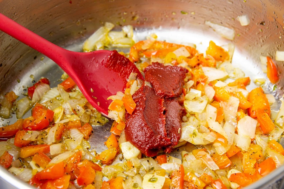 Añadir tomate concentrado y especias al sofrito de la caldereta de rape con langostinos