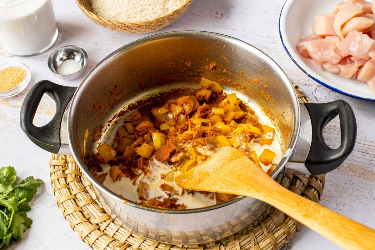 Añadir un poco de leche de coco para seguir rehogando la pasta del curry del pollo al curry con arro