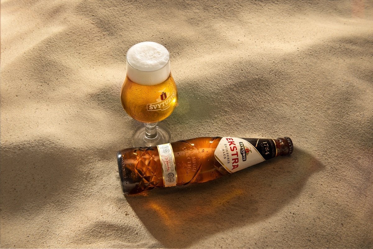 Botella y copa de Svyturys Ekstra tomando el sol en la playa