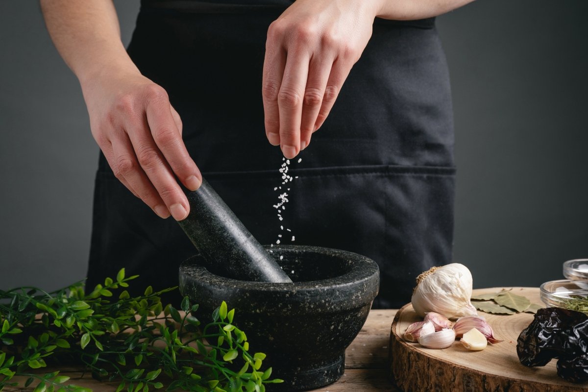Chef con delantal negro en una cocina echando sal en un mortero