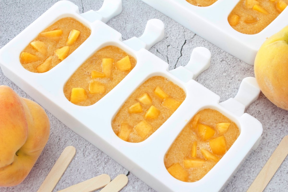 Placing pieces of peach in the molds to continue making the peach popsicles