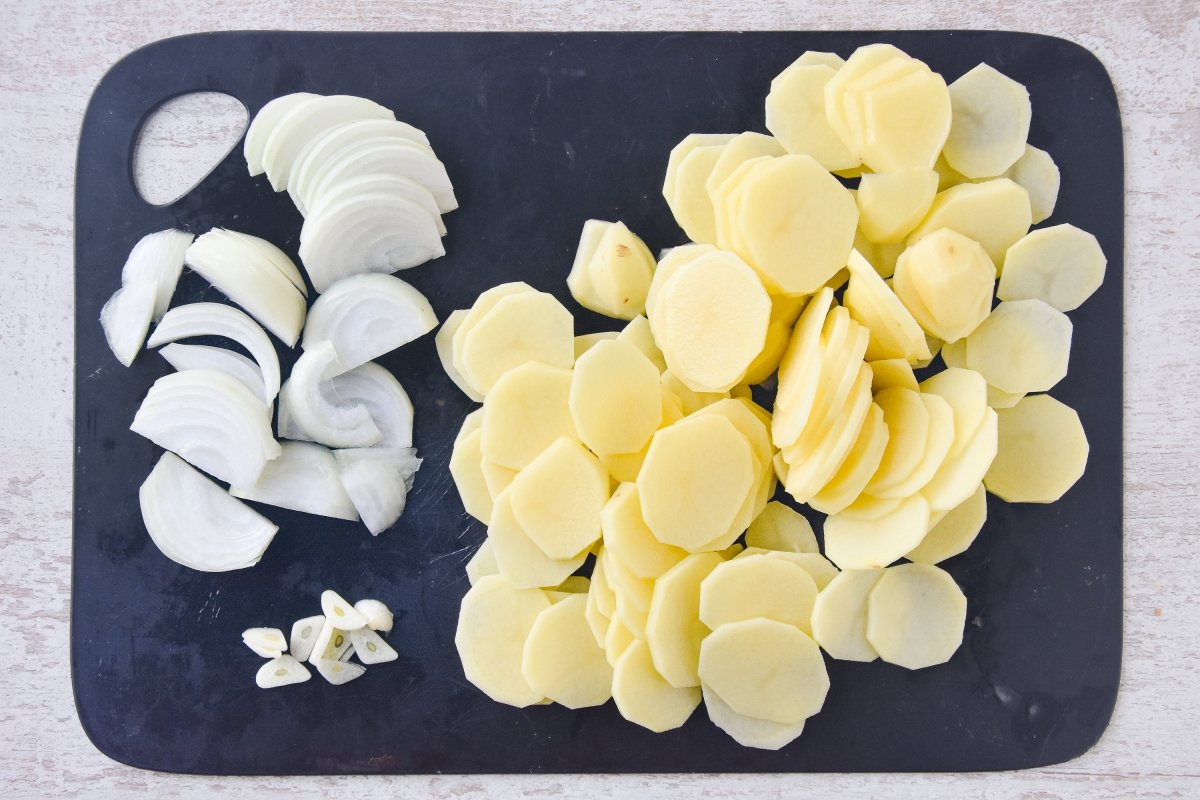 Cortamos las patatas, la cebolla y el ajo para hacer las patatas panaderas