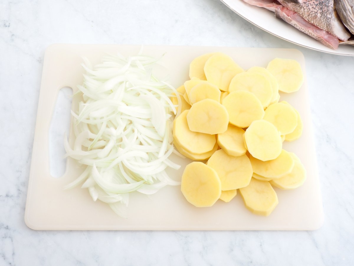 Cortar las patatas y cebolla para la corvina al horno