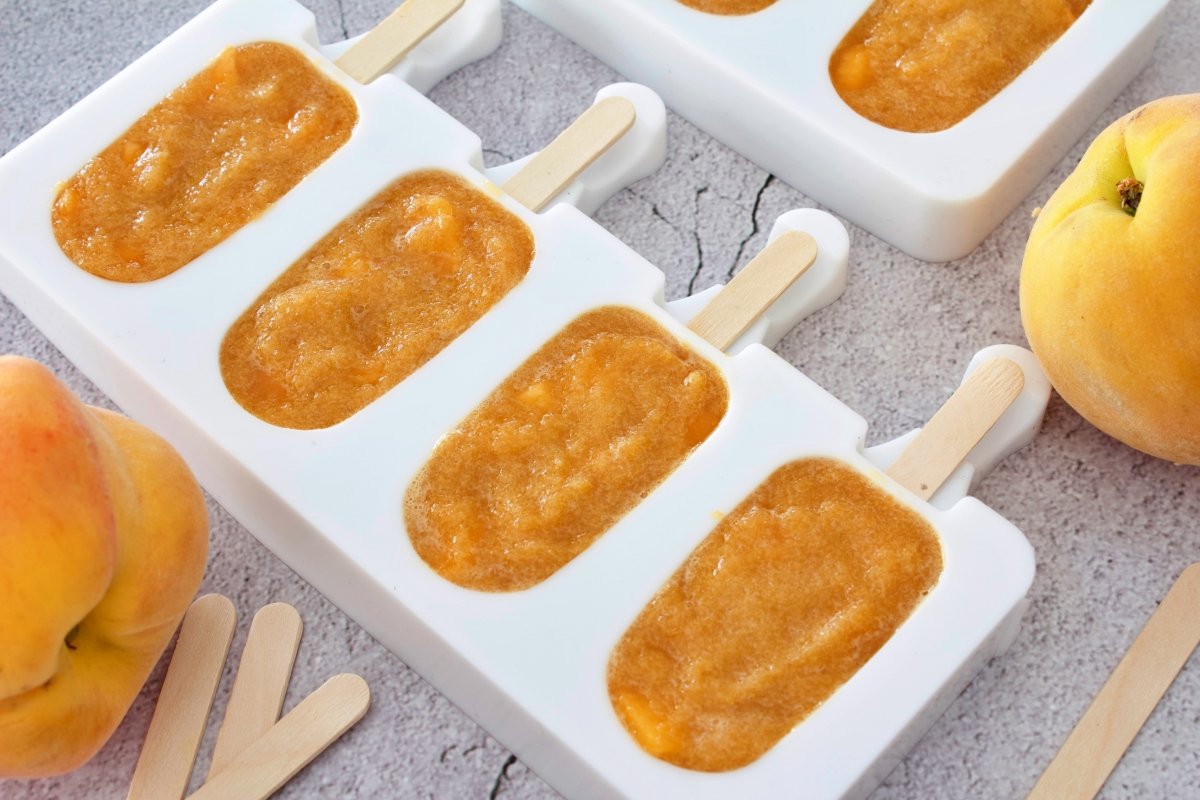 Covering the molds with crushed peach to continue making the peach popsicles