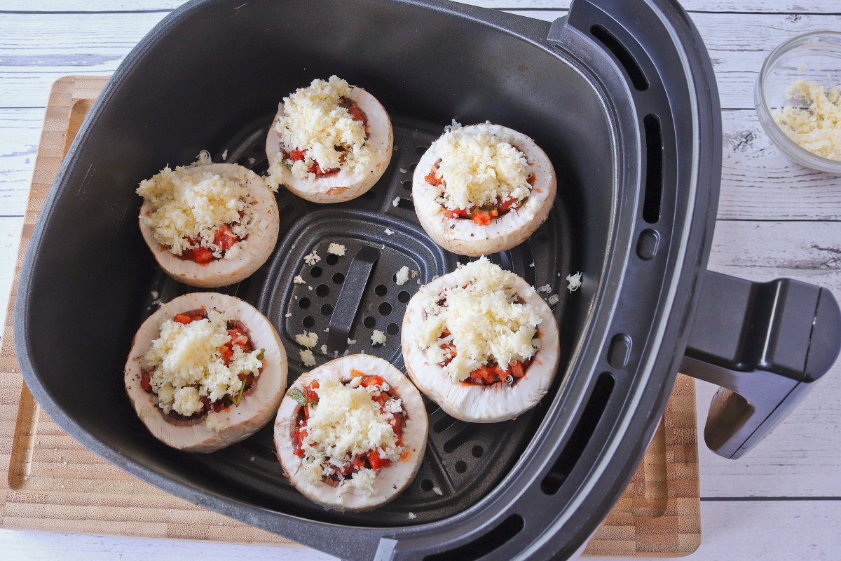 Cubrir con queso los champiñones rellenos y cocinarlos en la freidora de aire