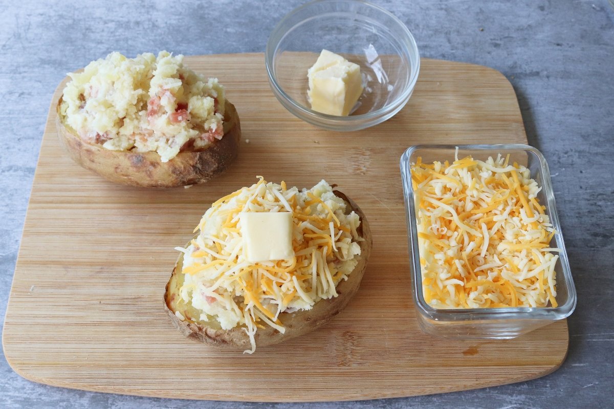 Cubrir con queso y mantequilla patatas rellenas de jamón y queso al horno