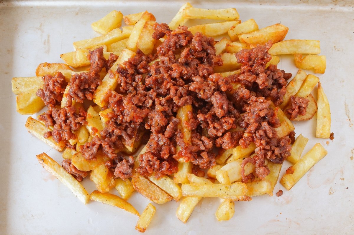 Cubrir las patatas fritas con el picadillo para la yaroa dominicana