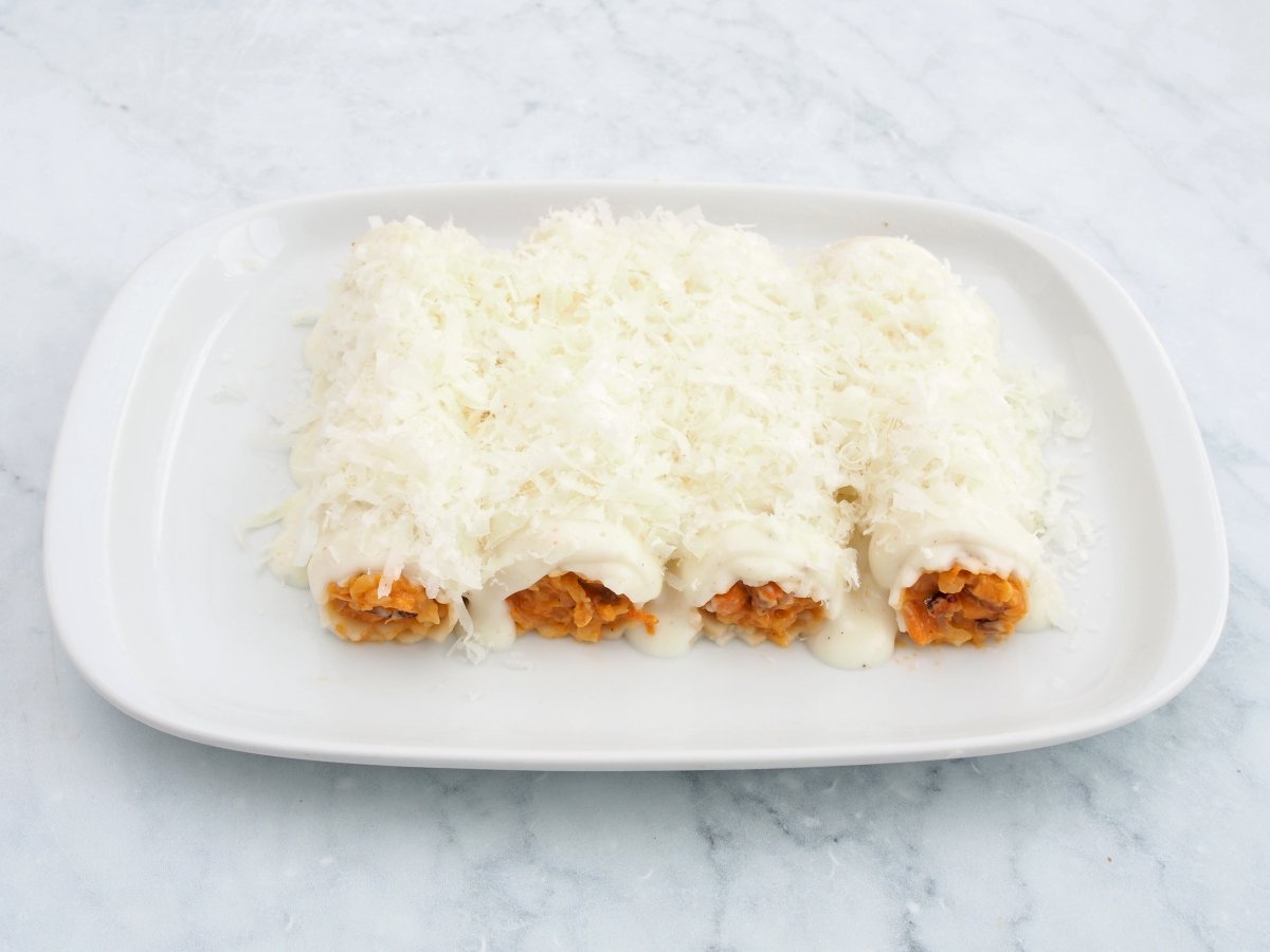 Cubrir los canelones de marisco con bechamel y queso rallado