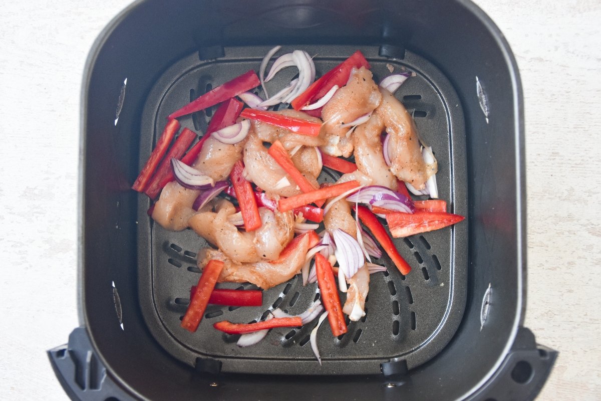 Disponemos el pollo con el pimiento y la cebolla en la freidora de aire