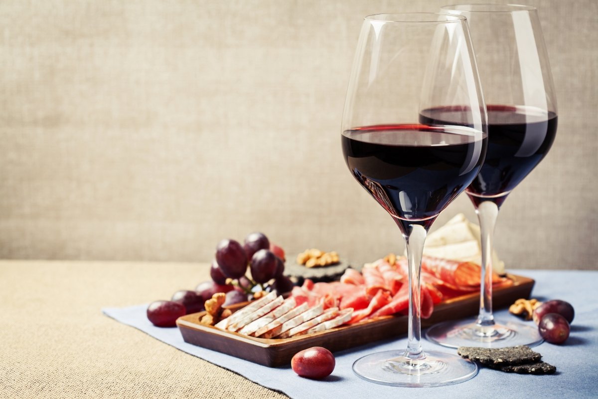 Dos copas de vino tinto con una tabla de embutidos y uvas rojas