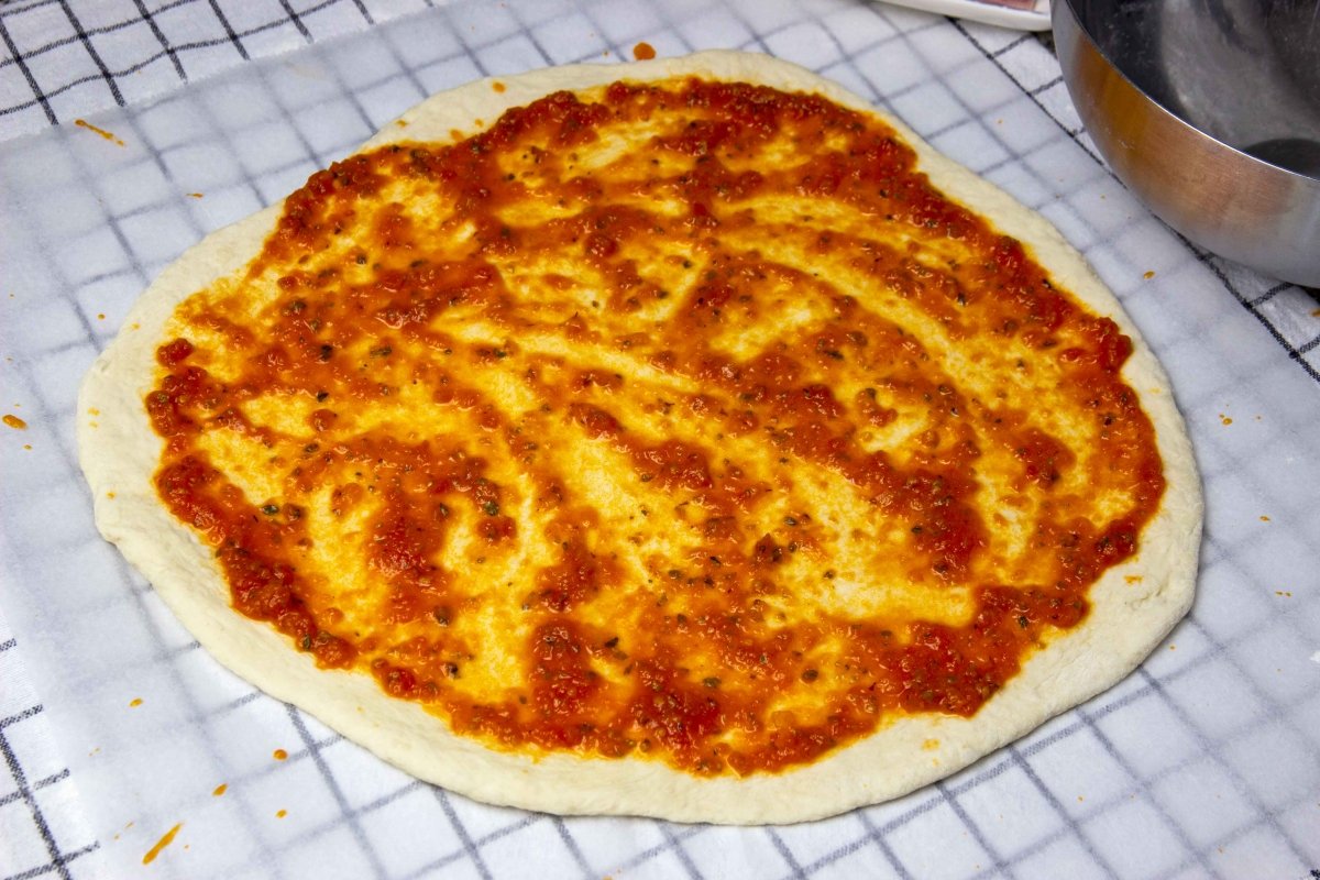 Echar salsa de tomate a la base para la pizza hawaiana