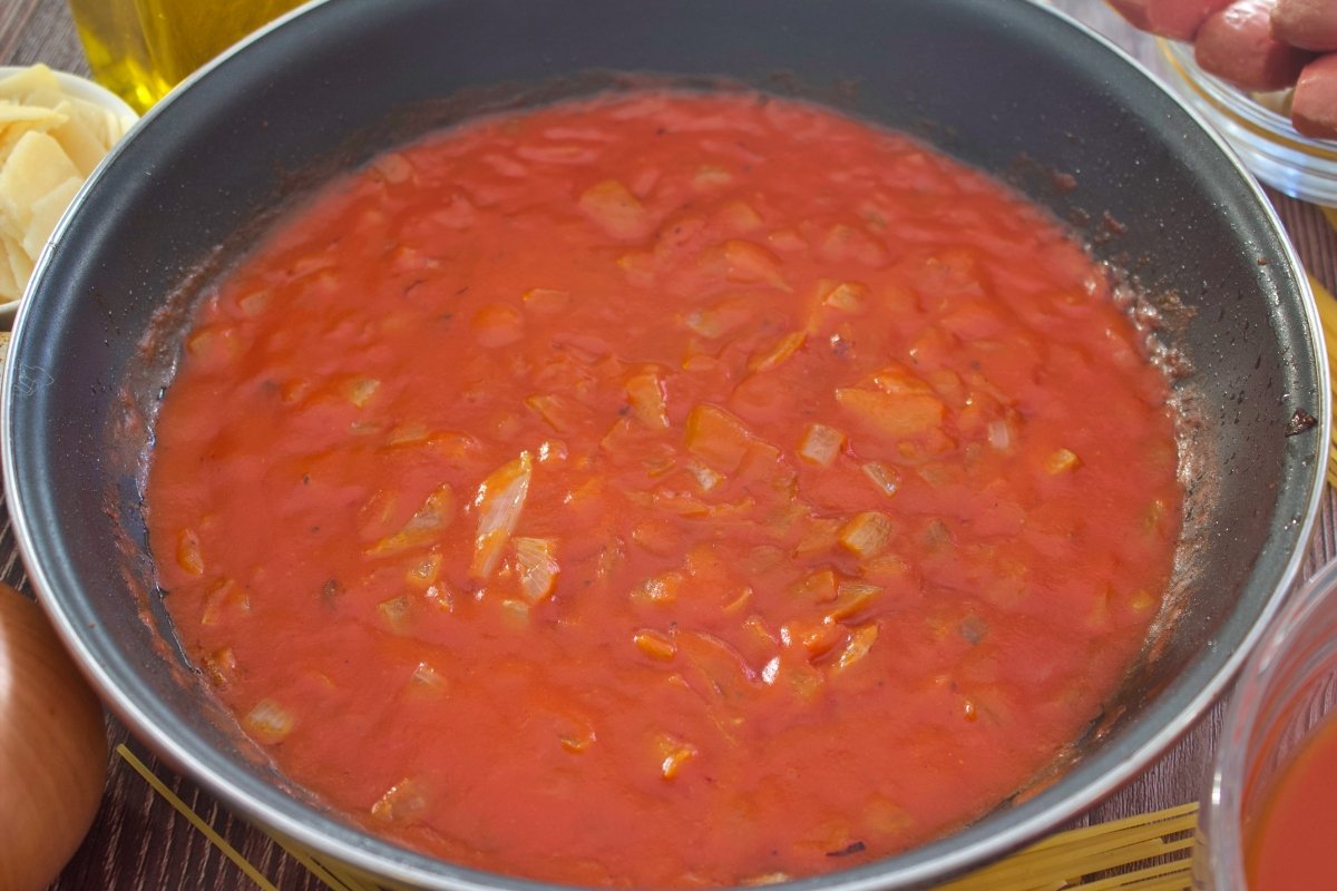 El tomate frito de los espaguetis con salchichas en la sartén