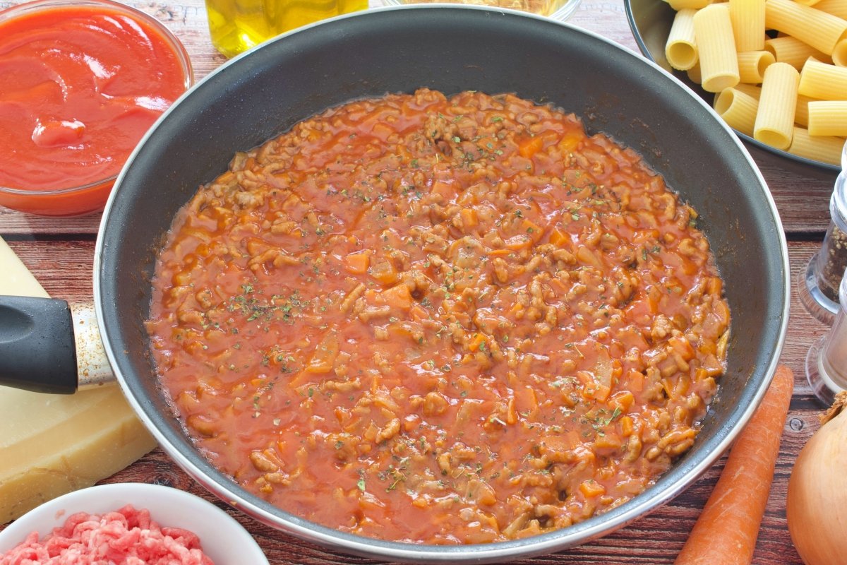 El tomate frito y el orégano agregados a la sartén de los rigatoni con salsa boloñesa