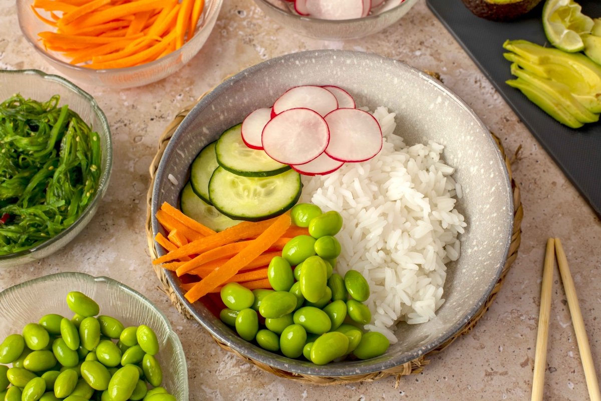 Empezar a montar el poke bowl de atún marinado y arroz por las verduras