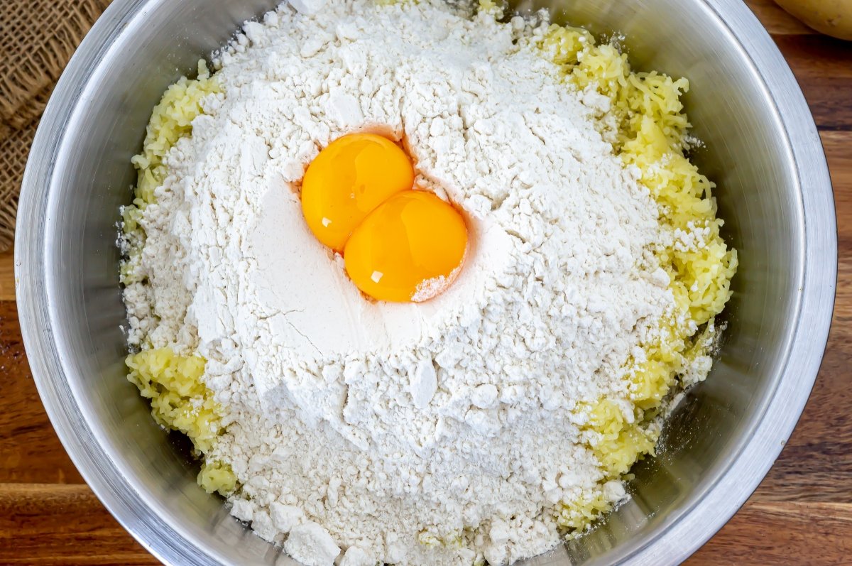 En un bol mezclar las patatas con la harina y los huevos ligeramente batidos