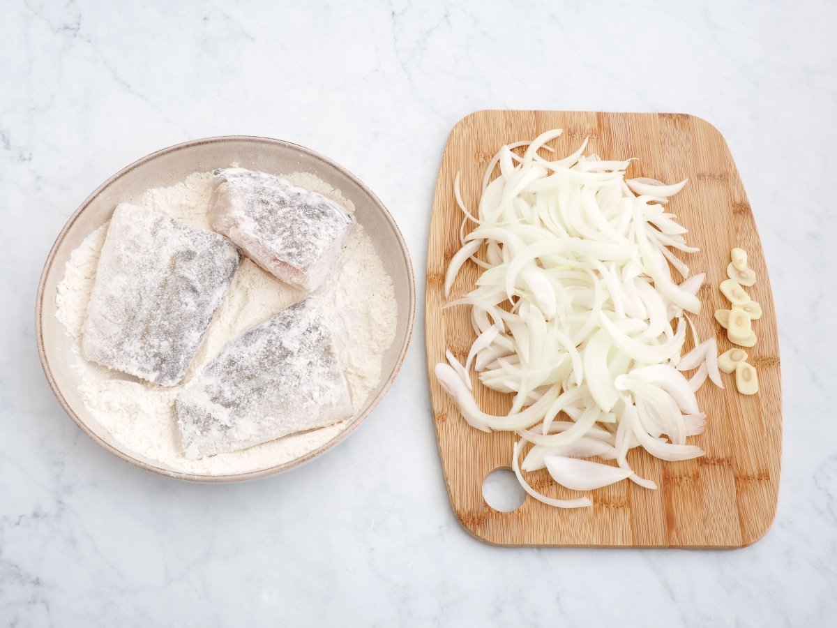 Enharinar el bacalao y cortar la cebolla y el ajo