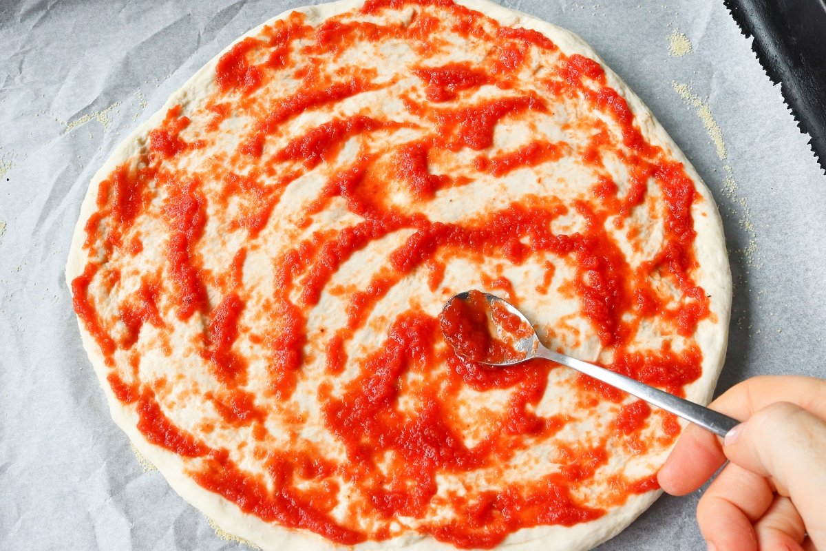 Extender el tomate sobre la pizza margarita