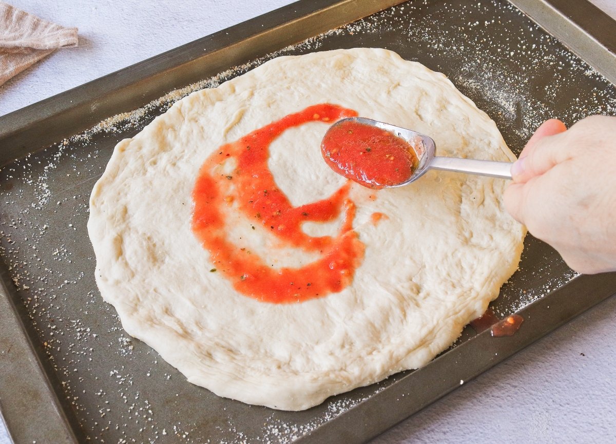 Extender la salsa de tomate sobre la pizza de queso de cabra y bacon