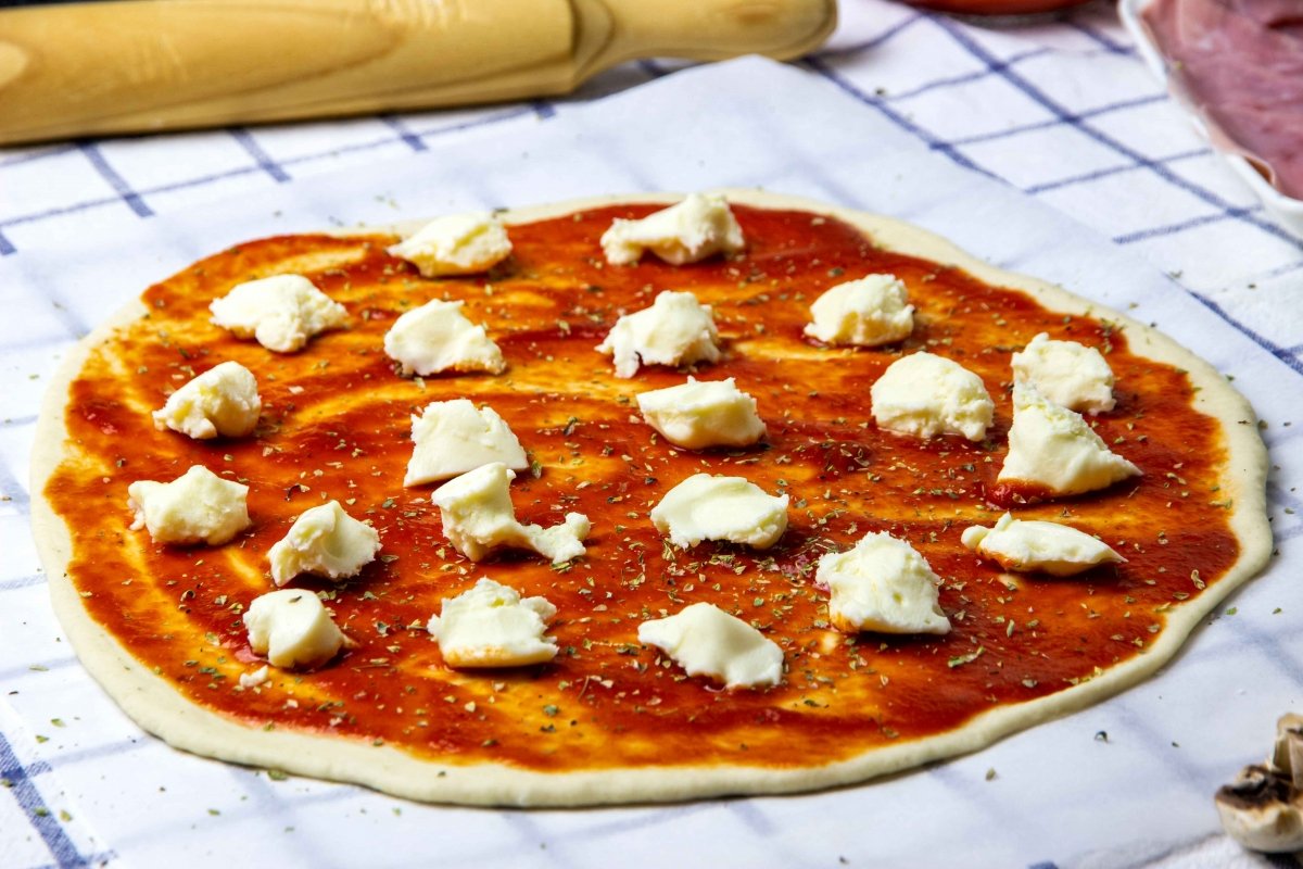 Extender salsa de tomate, orégano y mozzarella para hacer pizza romana