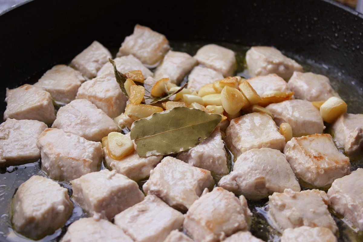 Incorporación de los ajos y el laurel a la sartén con los tacos de lomo de cerdo