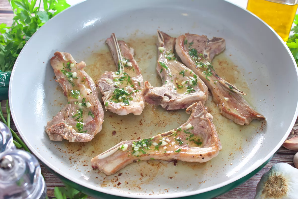 Las chuletas de cordero a la plancha en la sartén con la salsa por encima