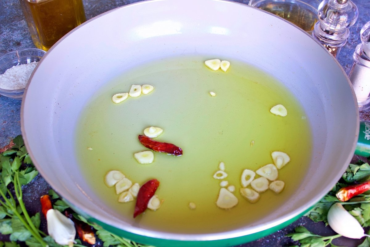 Las guindillas y el ajo de las cocochas de bacalao en salsa verde en una sartén con aceite
