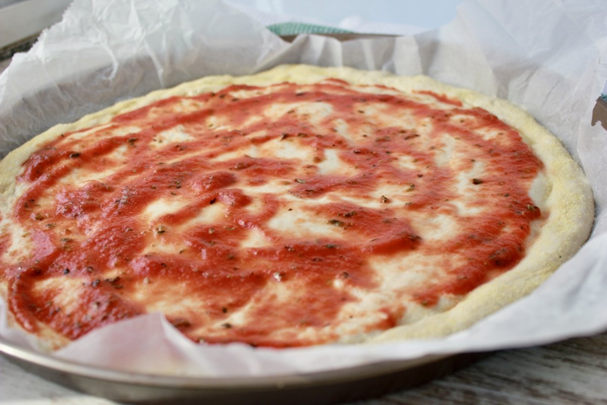 Masa de pizza cubierta con salsa de tomate y orégano