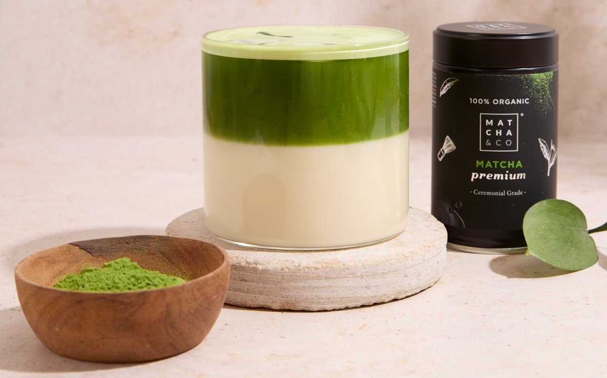 Matcha latte acompañado con un cuenco de matcha y una lata de matcha premium de Matcha & CO