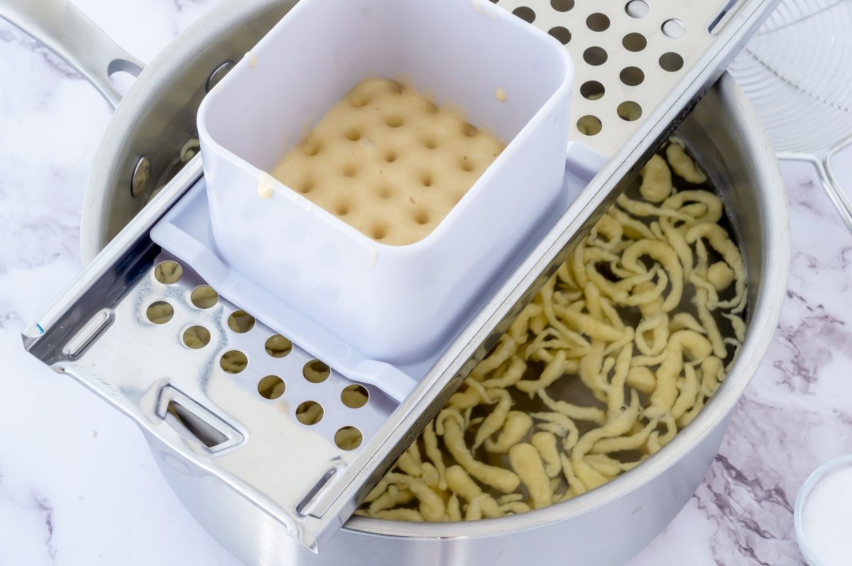 Pasar la masa de spätzle por la mandolina