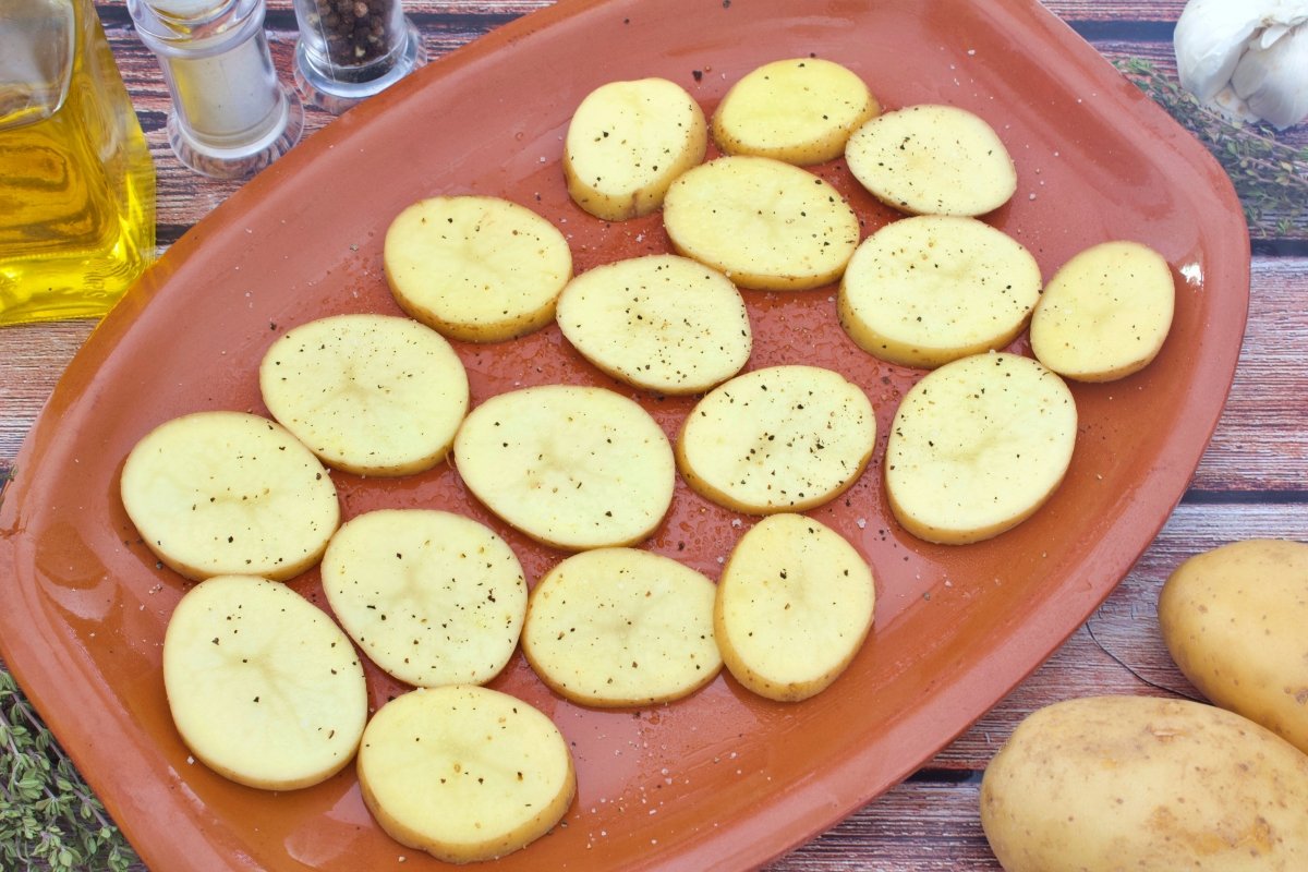 Patatas en rodajas sobre una bandeja de barro para el cabrito al horno con patatas